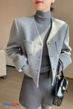 Person wearing a gray blazer with gold buttons, gray turtleneck, and gray pants, holding a black handbag.