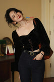Woman wearing a black velvet top and high-waisted pants indoors.