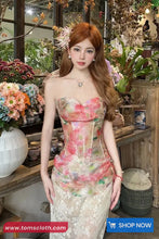 Woman in a floral dress standing in a decorative setting with flowers and plants.