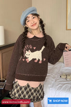 Woman wearing a brown sweater with a cat design, plaid skirt, and blue beret indoors.