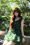 Woman in a green dress sitting by a pond with trees in the background