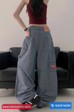 Person wearing oversized blue pants with a red top in a minimalistic setting.
