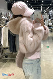 Person wearing a fluffy pink coat and light blue jeans in a store setting, taking a selfie.
