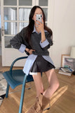 Woman taking a mirror selfie wearing a gray sweater, black skirt, and beige shoes in a room with a blue chair and white walls.