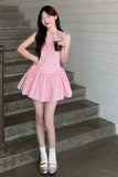 Woman in a pink checkered dress standing on stairs holding a drink.