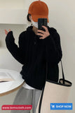 Person wearing a black hoodie, orange cap, and gray pants taking a mirror selfie.