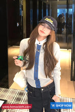 Woman wearing a cap and holding a product in a store setting with 'TomsCloth.com' branding.