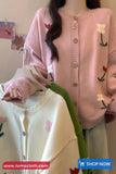 Person wearing a pink cardigan with floral embroidery holding a white cardigan.