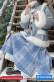 Person wearing a blue coat with white fur trim sitting on a wooden staircase outdoors.