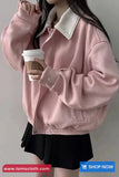 Person wearing a pink jacket holding a coffee cup against a plain background