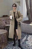 Woman in a beige trench coat standing outdoors holding a coffee cup.