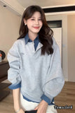 Woman wearing a gray sweater with blue collar and cuffs indoors