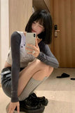 Woman sitting on the floor using a phone in a room with wooden flooring and a door.