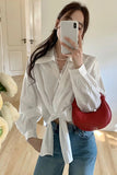 Person wearing a white shirt and blue jeans, holding a red handbag indoors.