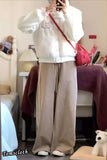 Person wearing a white hoodie with text and beige pants in a room.
