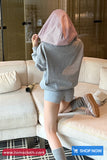 Person wearing a gray hoodie and shorts sitting on a couch with a checkered headscarf.