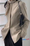 Person wearing a beige coat with a black handbag, standing against a light-colored wall.