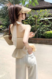 Woman in a yellow top and white pants walking outdoors with a straw visor and bag.