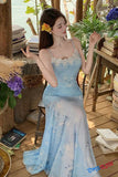 Woman in a light blue dress with floral patterns sitting in a cozy, wooden interior.