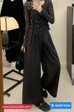 Person wearing a dark outfit with wide-leg pants in front of a mirror.