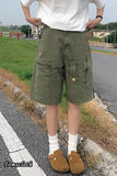 Person wearing green cargo shorts and white shoes on a road with grass and buildings in the background.