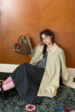 Woman sitting on a patterned rug holding a brown handbag against a wooden wall.