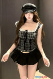 Woman wearing a black and white checkered top with a black skirt and cap against a plain background.