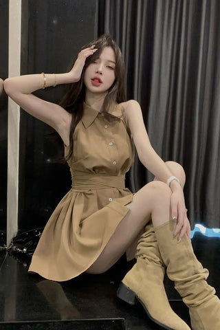 Woman in a beige dress and knee-high boots posing against a dark curtain.