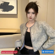 Person wearing a textured gray jacket over a black top in an indoor setting with a 'Shop Now' button visible.