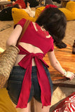Person wearing a red top with a bow detail and denim shorts in an outdoor setting.
