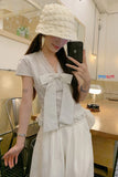 Woman taking a mirror selfie wearing a white hat and striped shirt with a bow in a room.