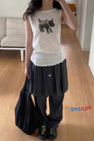 Person wearing a white sleeveless top with a dog design and black pants in a room.