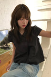 Woman wearing a black shirt and light blue jeans sitting indoors.