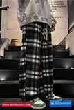 Person wearing plaid pants and a gray hoodie on a staircase with a visible brand logo.