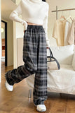 Person wearing a white cropped sweater and plaid pants in a room with a couch and clothes rack.
