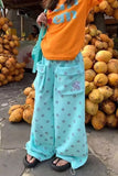 Person wearing an orange shirt and light blue pants with polka dots, standing in front of a display of fruits.