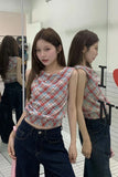 Woman wearing a plaid top and dark jeans standing in front of a mirror.
