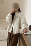 Person wearing a beige cap and white textured sweater in a room.