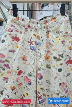 Floral patterned pants on a hanger with 'Toms Cloth' branding.