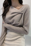 Person wearing a beige long-sleeve top with a draped design against a white background
