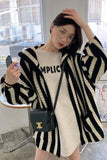 Person wearing a black and white striped cardigan over a beige t-shirt with text, holding a black handbag.