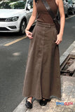 Person wearing a brown sleeveless top and long skirt on a street.