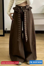 Brown wide-leg pants with plaid ruffle details on a wooden floor.