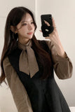 Woman taking a mirror selfie wearing a black dress with a brown bow and a brown patterned scarf.