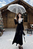 Woman in a black dress holding a transparent umbrella in front of a wooden cabin.