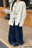 Person wearing a white cardigan with black buttons and dark blue pants on a wooden deck.