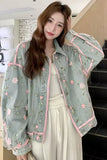 Woman wearing a light green floral embroidered jacket indoors.