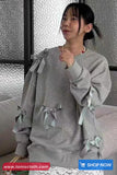 Person wearing a gray sweater with ribbons, sitting on a couch.