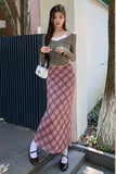 Woman wearing a green top and pink plaid skirt standing outdoors.