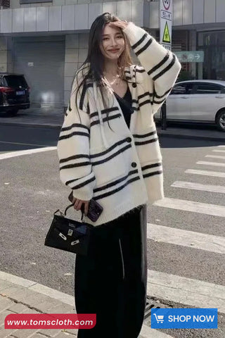 Woman wearing a striped cardigan on a street with a visible brand logo.